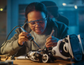 Young Teenage Multiethnic Schoolgirl is Studying Electronics and Soldering Wires and Circuit Boards in Her Science Hobby Robotics Project. Girl is Working on a Robot in Her Room. Education Concept.